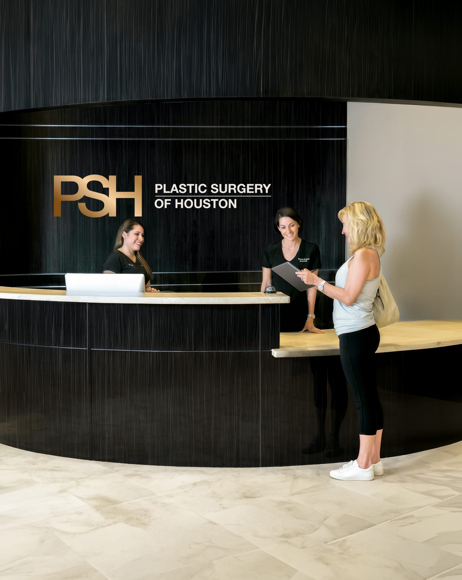 A patient at the Plastic Surgery of Houston reception desk, talking with two staff members
